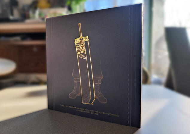 Photo of the back cover of the completed Crisis Core Scrapbook zine. It is facing away from the light source to better show the shine of the Spot UV and gold foil text. The background has been blurred to focus the image. Photo of the back cover of the completed Crisis Core Scrapbook zine. It is facing away from the light source to better show the shine of the Spot UV and gold foil text. The background has been blurred to focus the image.