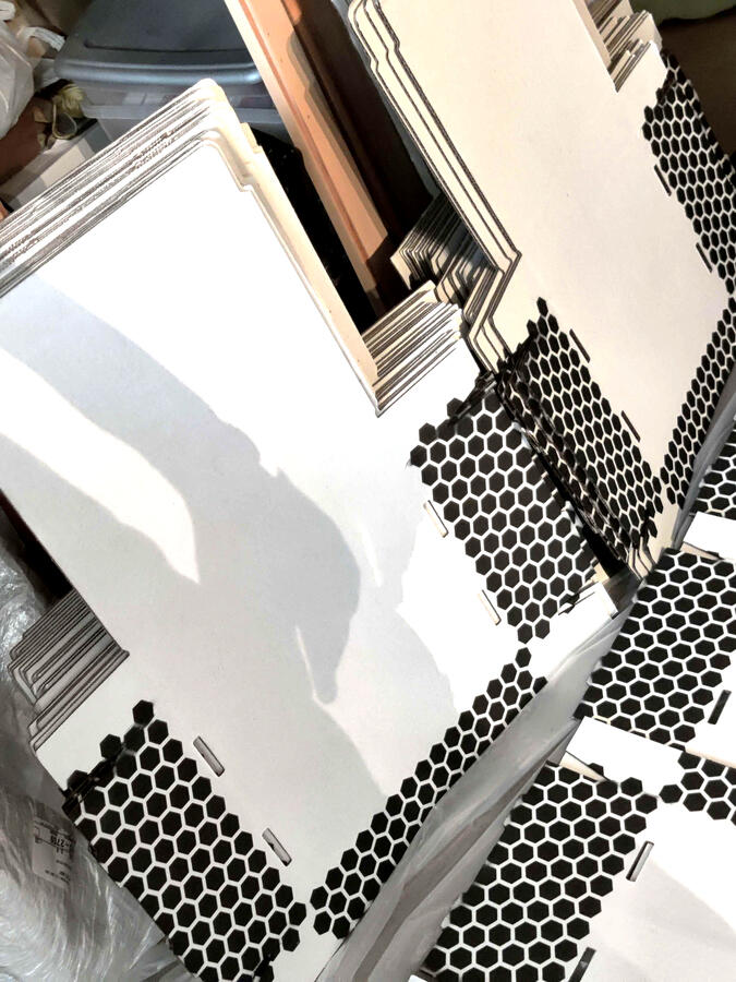 Stacks of unassembled white cardboard boxes with three sides patterned in black hexagon print.