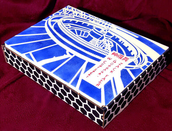 Healing Wave box. A stylized blueprint of Midgar (art by Krinxler + Guile) on the top with black hexagons on the sides. In red text on the lid are the kanji for &quot;Shinra Soldier&quot; and in English handwriting (font by @smulshinshin) is written &quot;ZACK FAIR, GONG