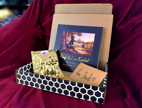 The box opened to show the scrapbook, merch package (in a Kraft paper newsprint bag with a sticker of the CCScrapbook logo by Frienduccine as a closure), and Aerith letter (design by Mary Woodard). The box opened to show the scrapbook, merch package (in a Kraft paper newsprint bag with a sticker of the CCScrapbook logo by Frienduccine as a closure), and Aerith letter (design by Mary Woodard).